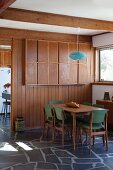 Pendant lamp with blue lampshade above 50s-style dining set in dining room with wooden partition wall and stone-flagged floor