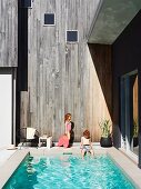 Children next to pool of Australian beach house against wooden facade weathered to a silvery grey