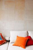 Scatter cushions with bright, velvet covers on pale couch against wall clad in sandstone tiles