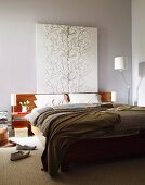 Painting of stylised tree above wooden headboard of double bed against grey-painted wall; designer standard lamp in corner