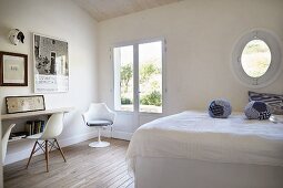 White bedroom with fabric spheres on bed and classic chairs to one side in front of French windows