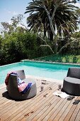 Cool off in the pool - dark brown rattan outdoor easy chairs on wooden deck next to pool in tropical garden
