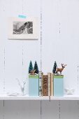 Hand-crafted bookends with winter motifs decorated with miniature deer and tiny fir trees on shelf on white, wooden wall