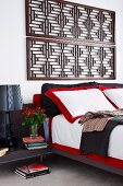 Ausschnitt eines Doppelbettes mit rot-weisser Bettwäsche, vor Wand mit montierten, antiken Holzgittern