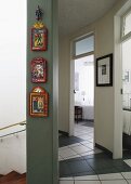 Colourful panels hanging in vertical row on wall in hallway with tiled floor and curved wall; view into neighbouring rooms through open doors