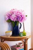 Pink flowers in blue jug on console table made of bent bamboo