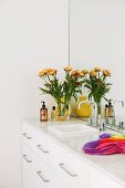 Weißer Waschbeckenunterschrank mit raumhohem Wandspiegel und gelbem Blumenstrauß in Designer Ambiente