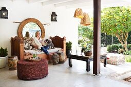Relaxing on a veranda; woman and dogs on antique bench, rattan pouffe and view into garden to one side