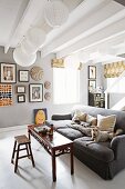 Antique bench in front of dogs on grey sofa in rustic living room with several spherical paper lampshades hanging from white wood-beamed ceiling