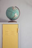 Alter Globus auf weißem Vintage Spind mit pastellgelb lackierten Türen