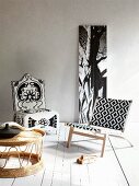 Stoffbespannter, moderner Holzsessel mit grafischem und Polsterstuhl mit floralem Muster vor Baumstammfoto, im Vordergrund ein Geflechttisch