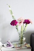 Venetian mask and glass vase of purple carnations and delicate pink gerbera daisies on white side table