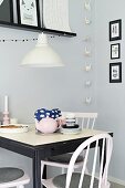 Small, black and white dining area in front of grey-painted wall with origami garland and gallery of black-framed pictures
