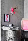 Hunting trophy painted neon pink above printed number on concrete wall above barrel-shaped table made from hammered metal