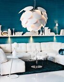 Weiß möblierte Sitzecke - Designer Hängeleuchte mit schuppenartigem Schirm über Sofalandschaft, dahinter Wandbord mit Spotbeleuchtung an blau gestreifter Wand