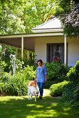 Woman and dog in summery garden in front of white, weatherboard country house with veranda