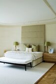 Double bed with upholstered, tall, pastel grey headboard in elegant bedroom with stucco ceiling and white rug