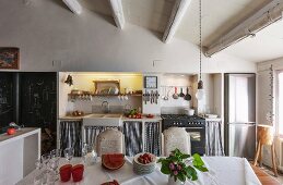 Dining table with white tablecloth opposite kitchen counter in rustic dining area with wood-beamed ceiling