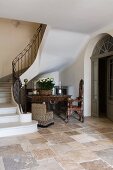 Foot of staircase with wrought iron balustrade, stone floor and antique furniture in historical, French country house