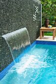 Waterfall emerging from screen of stacked stones next to pool