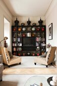 Pale armchairs in front of ceramic vases and TV on dark wooden shelving in living room