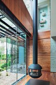 Suspended, cast iron fireplace in contemporary house next to glass facade with view of garden