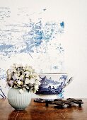 White, spherical vase of hydrangeas and white and blue painted bowl (toile de jouy) against wall with blue plant-like structure on white background