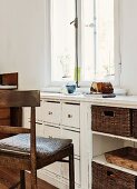 Old wooden chair with seat cushion in front of custom, vintage base units with drawers below window
