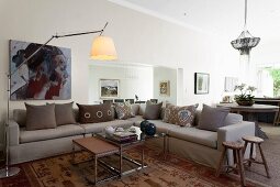 Nest of coffee tables and pale grey corner sofa with colour-coordinated scatter cushions in open-plan interior