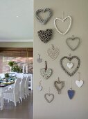 Various love-hearts made from different materials on grey-painted wall; view of set dining tabla and white rattan chairs to one side