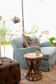 Round, ethnic side table next to pale grey couch and retro standard lamp; garden view