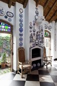 Antique chairs flanking tiled fireplace below decorative plates on walls; open terrace doors leading to courtyard on either side
