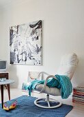 Pale blue blanket on white swivel armchair and modern artwork on wall