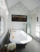 Bathroom with free-standing vintage bathtub below window in attic bathroom with white and grey wallpaper