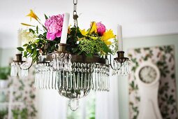 Summer flowers on chandelier with glass droplets and white candles suspended from ceiling