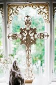 Ornate crucifix made from white-painted metal in front of window
