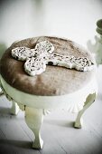 Ornate, white, vintage cross on footstool with cushion