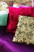 Silk-effect, gold cushion with pattern of roses and red plush cushion on purple couch