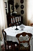 Chairs with carved backrests around round table with white tablecloth in corner of traditional interior