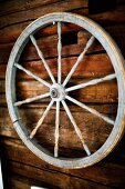 Old cart wheel with turned spoked hanging on wooden wall
