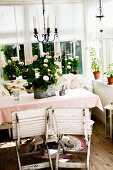 Weathered, wooden folding chairs painted white in front of potted plants on tablecloth on table in corner of loggia