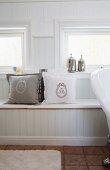 Monogrammed scatter cushions on window seat with storage space in white, country-house bathroom