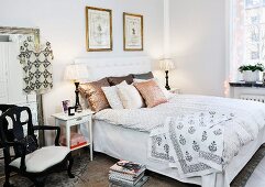 Double bed with collection of scatter cushions against upholstered headboard and table lamps on white bedside tables in rustic bedroom
