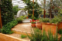 Mediterraner Flair in einem Garten durch Terrakottatöpfe, Pflaster und Steinbrunnen mit Löwenkopf