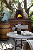 Wine glasses and carafe on bistro table in front of blazing fire in masonry pizza oven