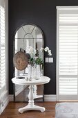 Orchids on white, round side table in front of arched, full-length mirror against dark wall