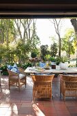 Rattanstühle und Holztisch auf Terracotta-Terrasse und Garten im Hintergrund