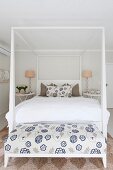 Double bed with white four-poster frame and bench with floral white and blue upholstery at foot