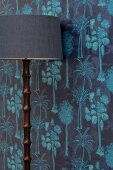 Standard lamp with wooden base against wallpaper in shades of blue with pattern of coconut palms
