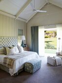 Double bed with button-tufted headboard, arranged scatter cushions and blanket; open terrace doors with a view to one side